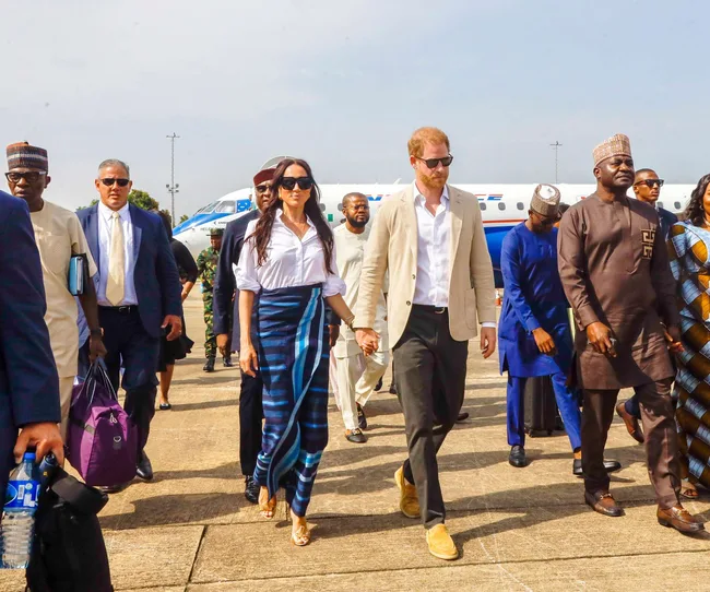 Harry & Megan walking on tarmac with plane behind them