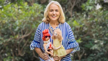 Jill Armstrong holding a few of her dolls in front of a bush