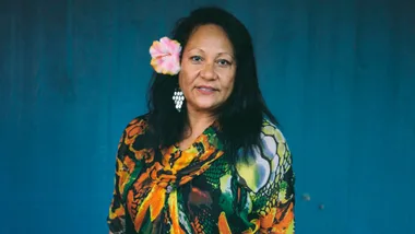 Ruth Aickin smiling in front of a blue backdrop with a flower in her hair