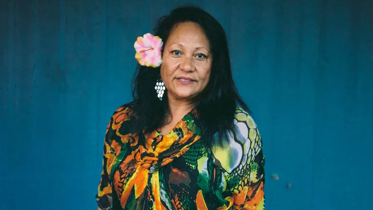 Ruth Aickin smiling in front of a blue backdrop with a flower in her hair