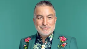 Dai Henwood in front of a turquoise backdrop in an embroidered turquoise suit