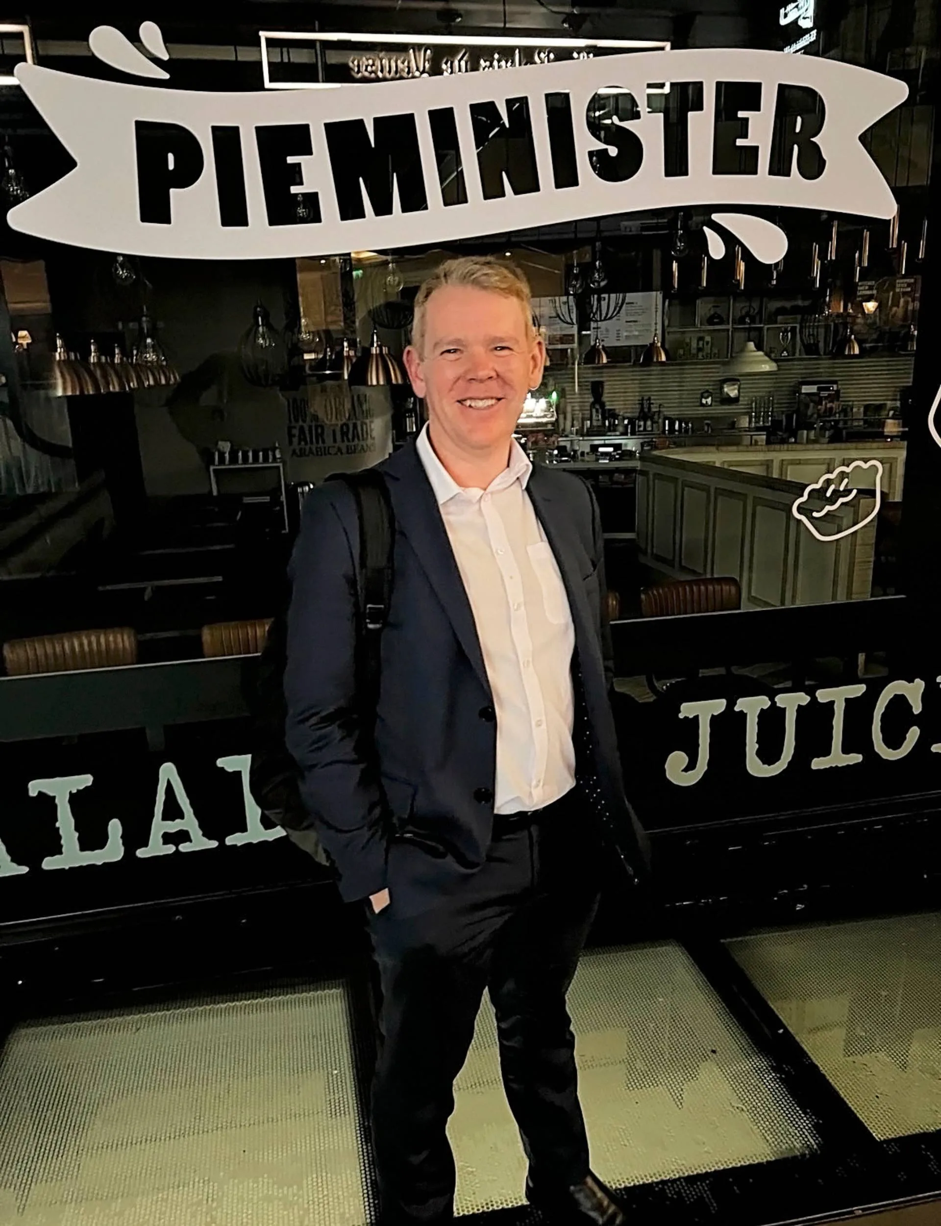 Chris Hipkins in front of a bakery named 'Pie Minister'