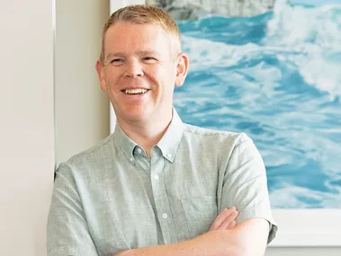 Chris Hipkins leaning against a white wall with his arms crossed