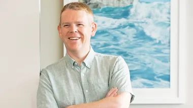 Chris Hipkins leaning against a white wall with his arms crossed