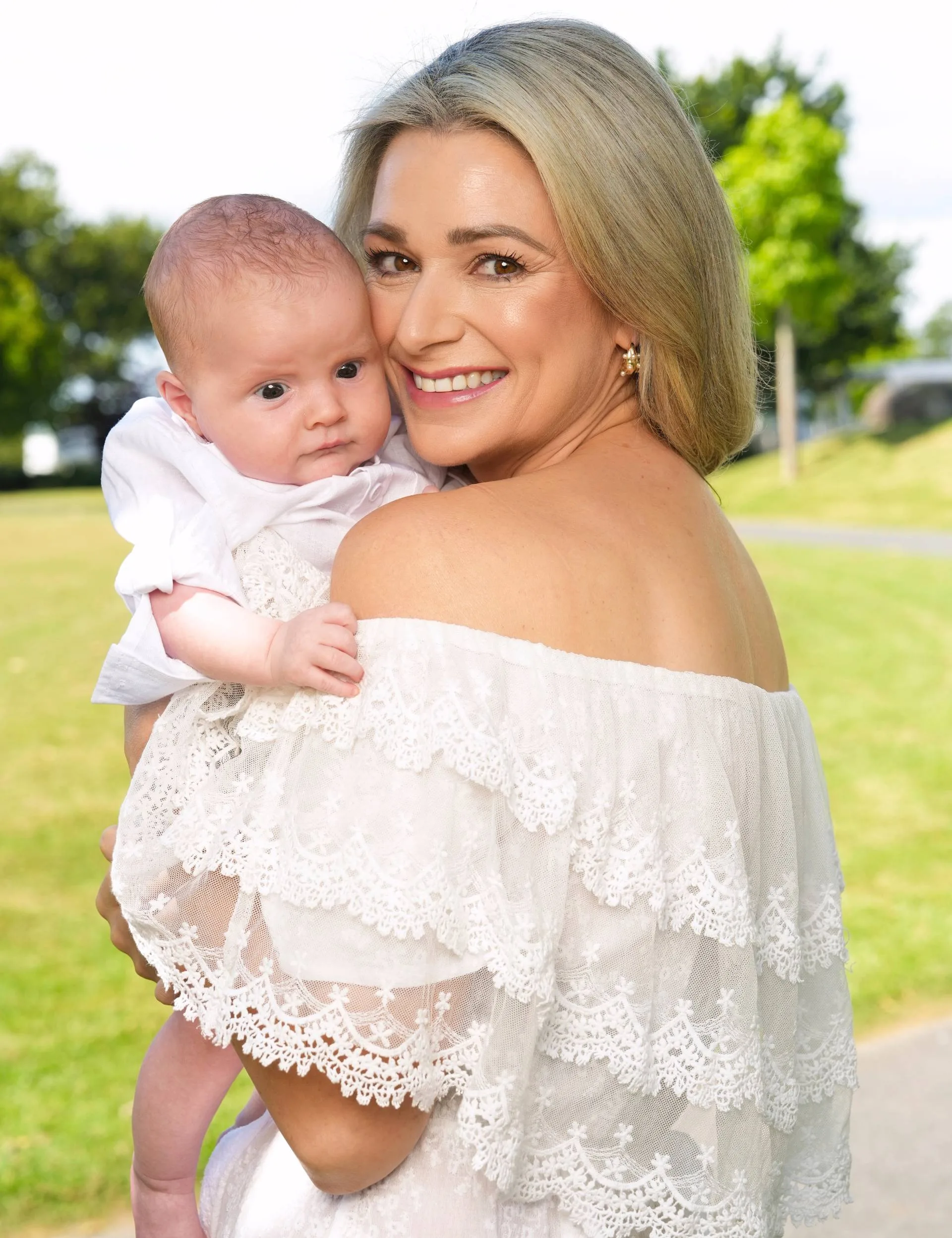 Erin looking over her shoulder while holding baby Harley in a park outside