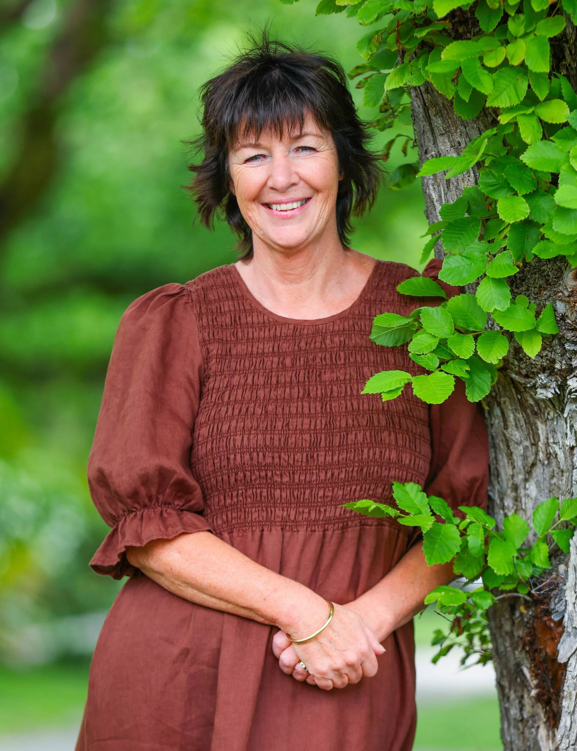 middle-aged woman wearing brown dress leaning against a tree