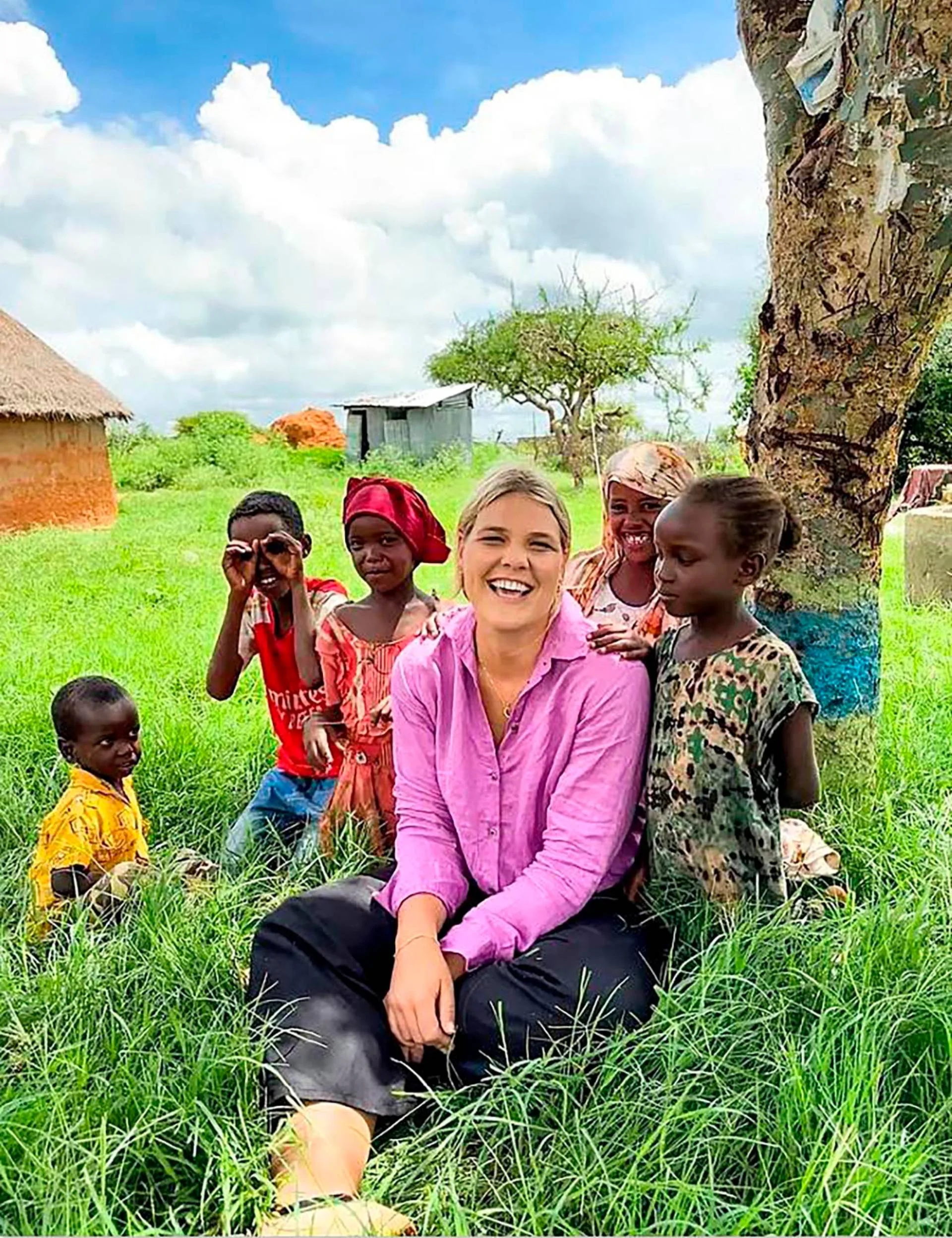 blonde woman sitting under a tree with children surrounding her