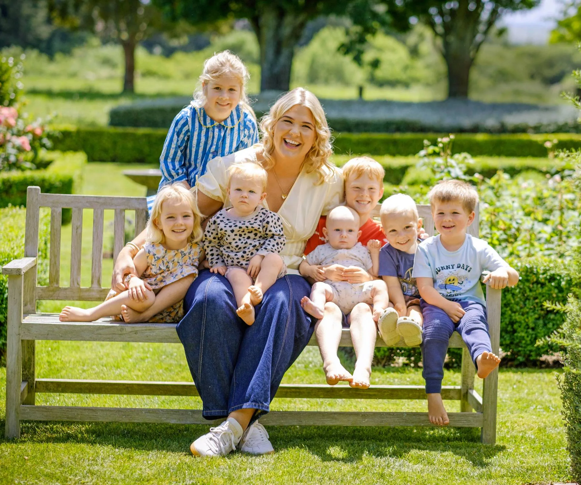 Young woman with 7 children sitting on a bench in a garden