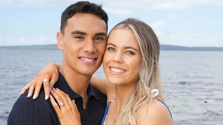 Max Mata and Greer Sinclair posing on a beach showing off the engagement ring