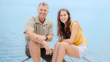 Steve and Riley sitting on the tip of a boat in front of the ocean