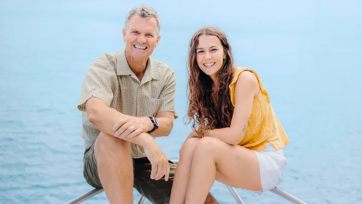 Steve and Riley sitting on the tip of a boat in front of the ocean