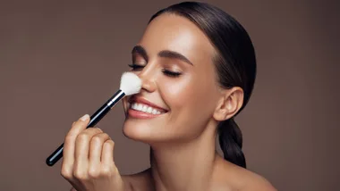 Woman wearing make-up with brown background and she's holding a make-up brush that she received as one of her Valentine's Day gifts