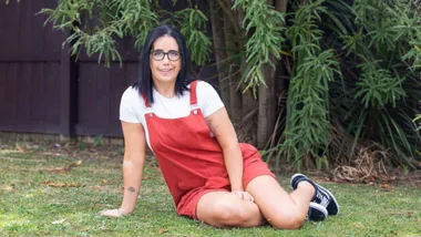 Grace Archer wearing red dungarees sitting on some grass outside