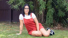 Grace Archer wearing red dungarees sitting on some grass outside