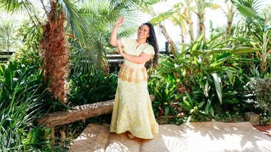 Indira Stewart in a yellow dress doing a traditional dance in front of lush greenery