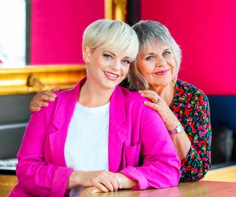 Laura Hill and Ginette McDonald standing next to each other wearing bright pink and bright florals