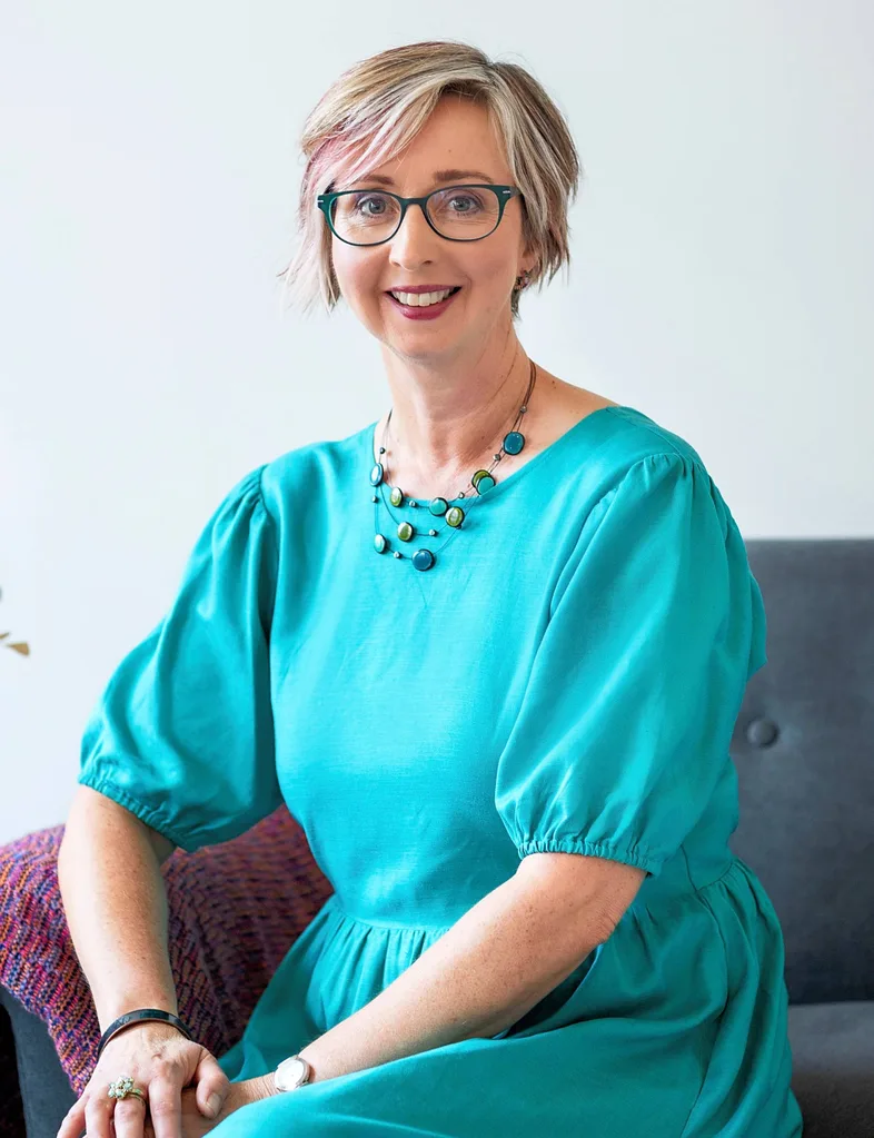 Lady seated wearing a blue dress with short hair smiling at camera