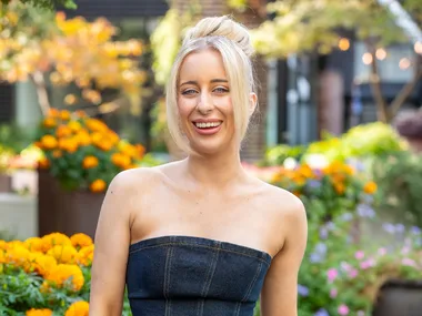 MAFS Jamie wearing denim jumpsuit with potted yellow flowers in background