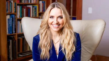 Mel Homer sitting on a white armchair in a velvet blue suit