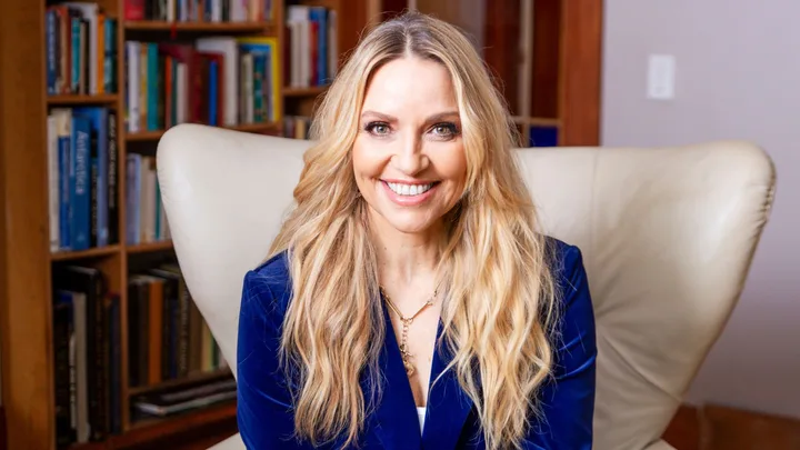 Mel Homer sitting on a white armchair in a velvet blue suit