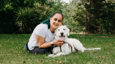 Ocean Armstrong crouching in the grass beside her guide dog