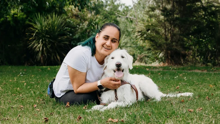 Ocean Armstrong crouching in the grass beside her guide dog