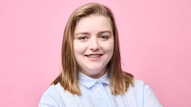 Maxine Scheckter smiling in her apron in front of a pink backdrop