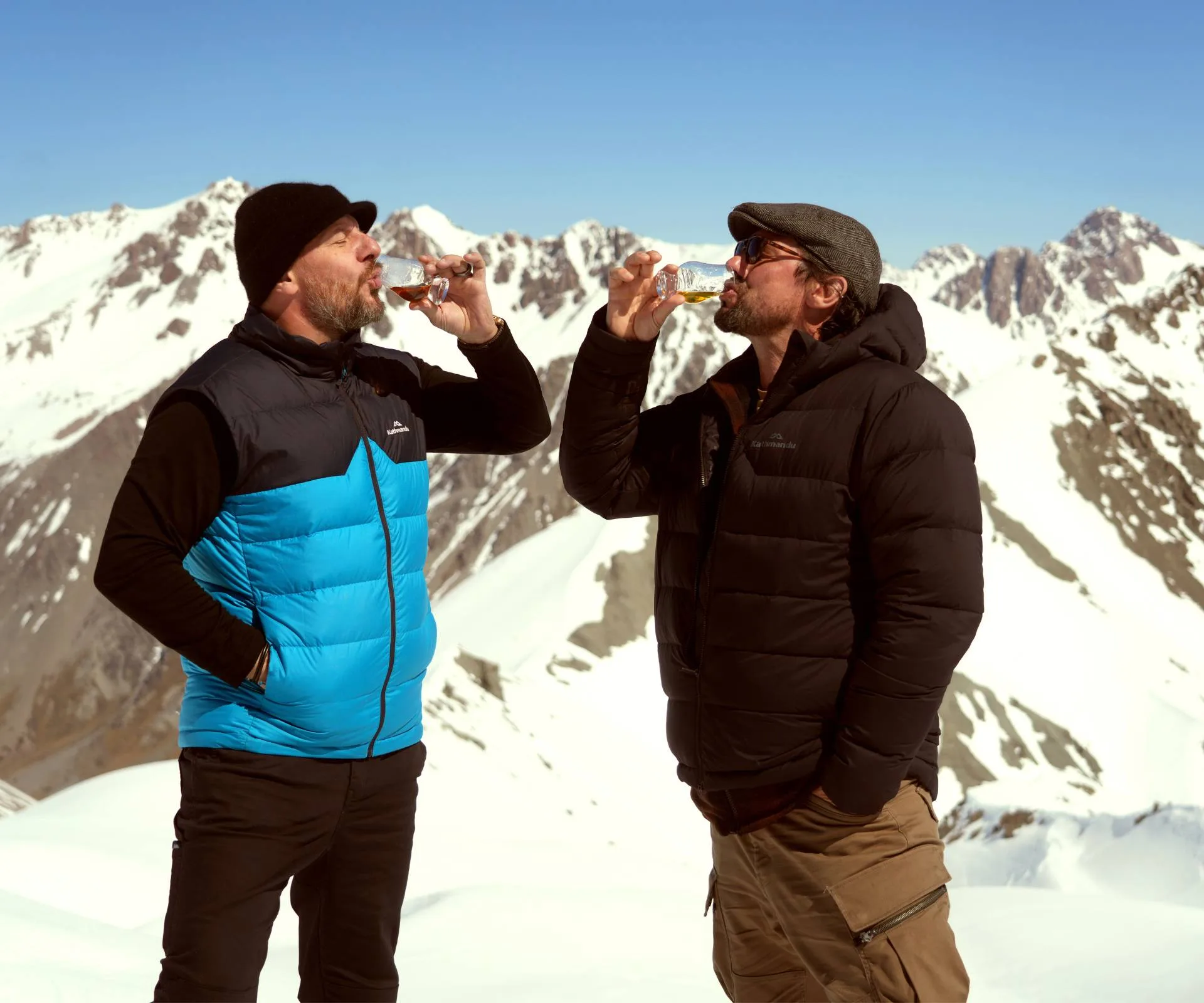 Colin and Manu drinking whiskey in front of snowy New Zealand mountains
