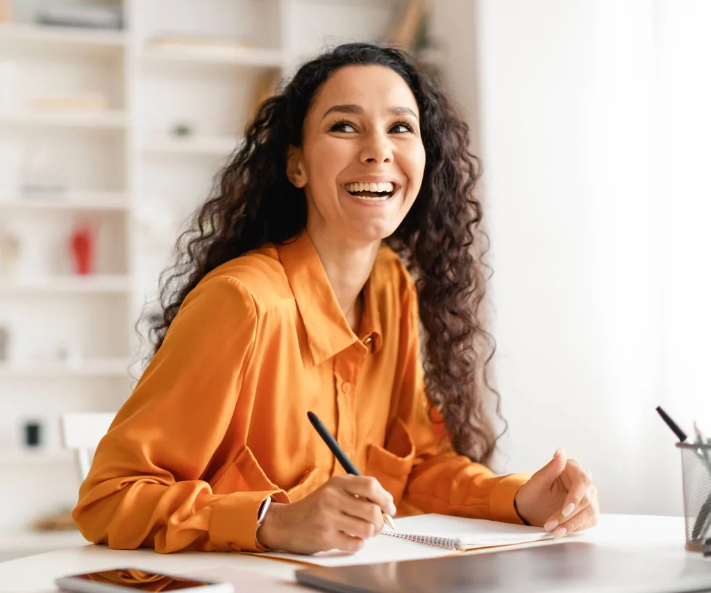 A woman smiling while writing at her desk because the yes effect worked
