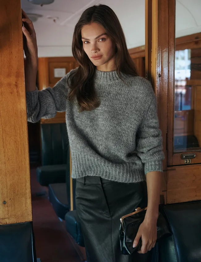 Model wearing grey high necked jumper and black leather skirt