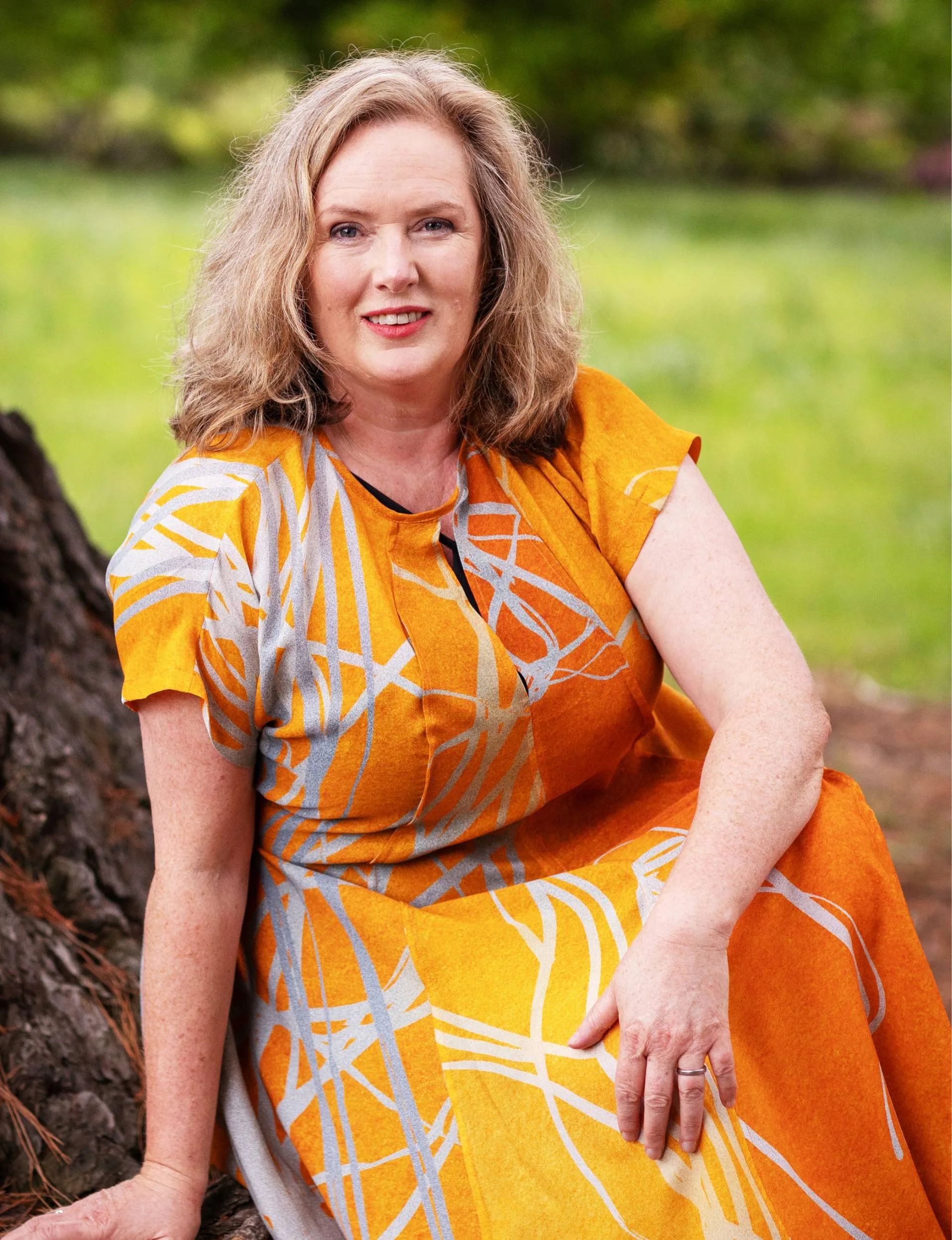 Lara Macgregor sitting at the base of a large tree in an orange dress