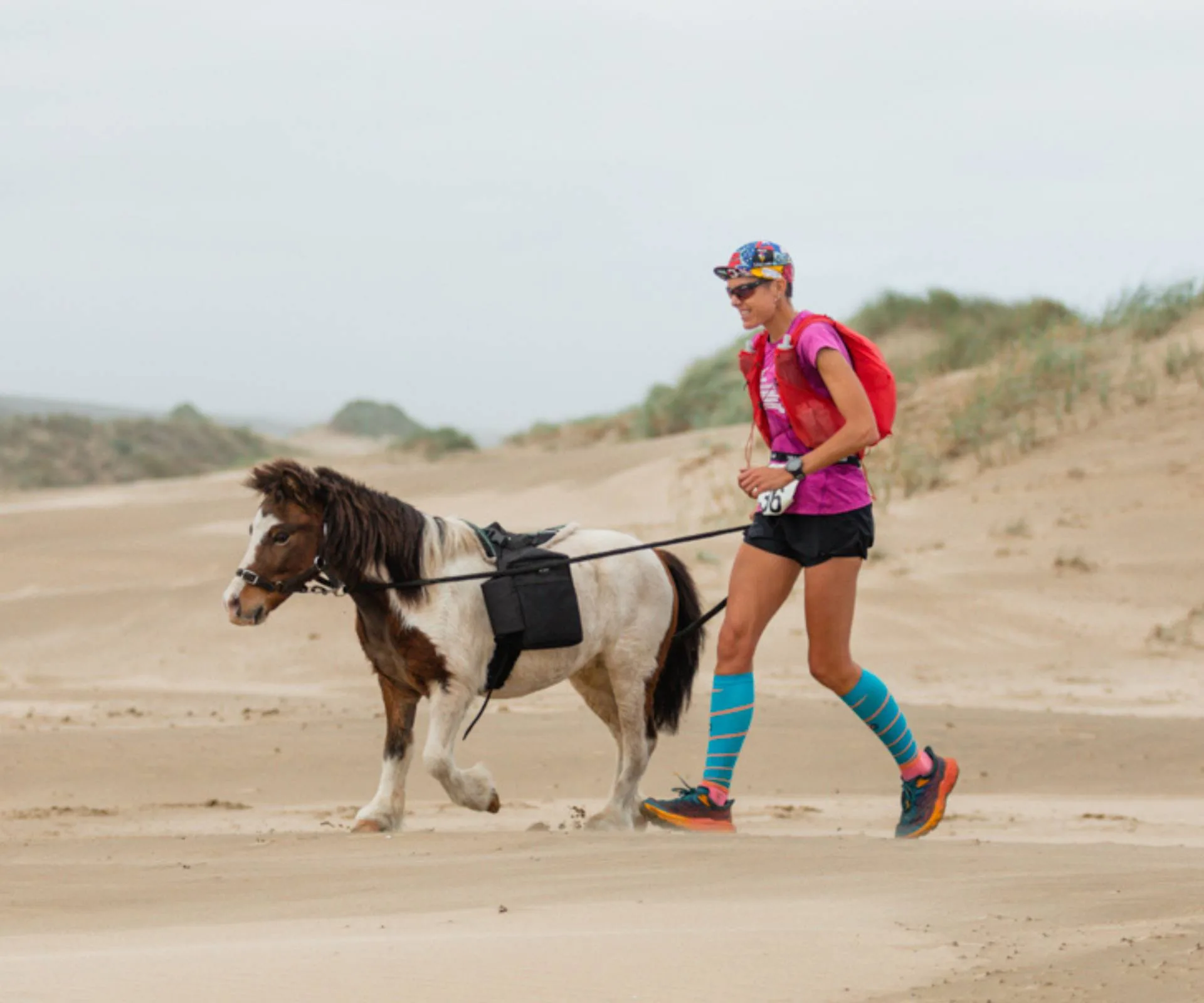 Chloe Phillips-Harris running in a desert beside a miniature horse