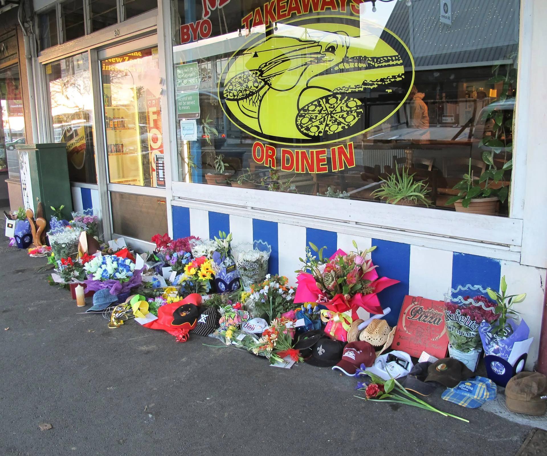 flowers and memorial pieces laid against the front of the takeaway store