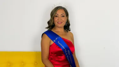 Delilah Whaitiri sitting on the arm of a yellow sofa in her Miss Aotearoa sash and crown