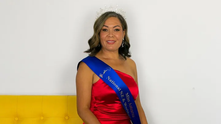 Delilah Whaitiri sitting on the arm of a yellow sofa in her Miss Aotearoa sash and crown