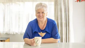 Jo Duston sitting at her kitchen counter with a cup of tea