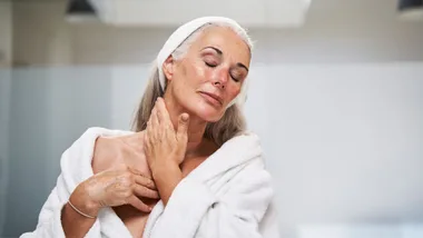 Woman with eyes closed massaging neck in bathroom