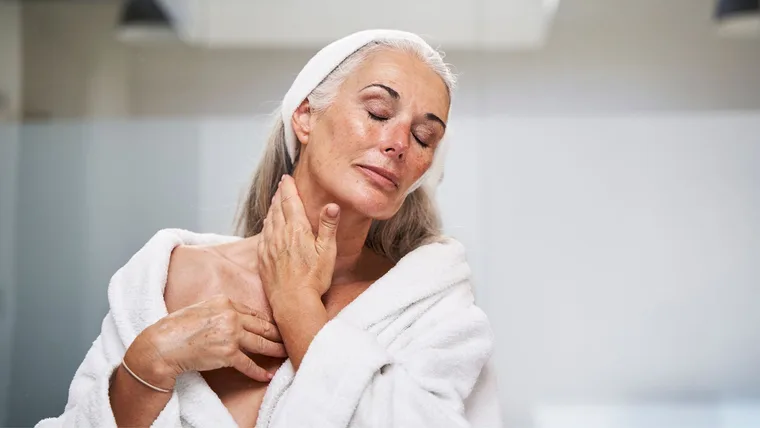 Woman with eyes closed massaging neck in bathroom