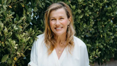 Robyn Malcolm sitting in front of a hedge