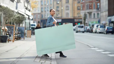 Lady walking across the street holding giant paper shopping bag