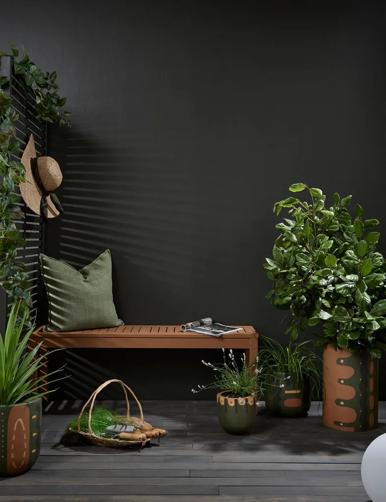 A winter staycation can be as simple as creating a cosy sheltered spot outside. This room has a dark wall and deck with brown furniture and lots of plants