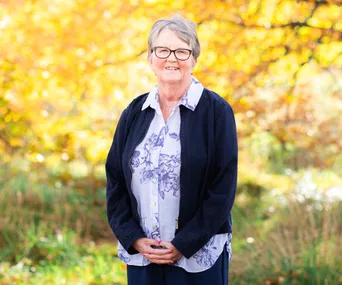 Kim Hewson wearing shirt and cardigan with autumn leaves in background