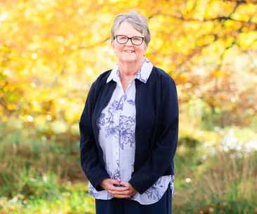 Kim Hewson wearing shirt and cardigan with autumn leaves in background
