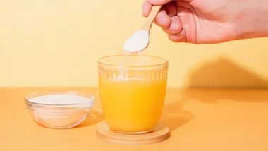 A powder supplement being sprinkled into orange juice