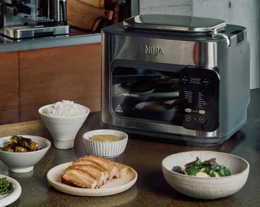 ninkja combi multicooker on bench with plates and bowls of food