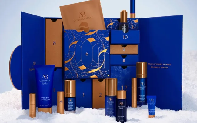 Luxurious skincare advent calendar with blue and gold box design, various compartments, and skincare products, all on a snowy white surface.