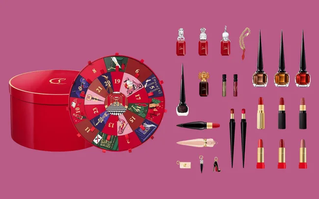 Red and gold round box with an advent calendar wheel displaying the days and images. Assortment of luxury beauty products set against a pink backdrop.