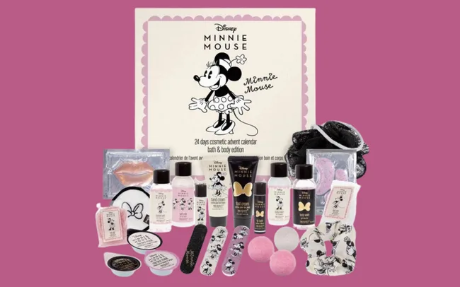 Minnie Mouse-themed bath and body advent calendar with various cosmetics and accessories against a pink background. Includes lotions, bath bombs, and lip balm.