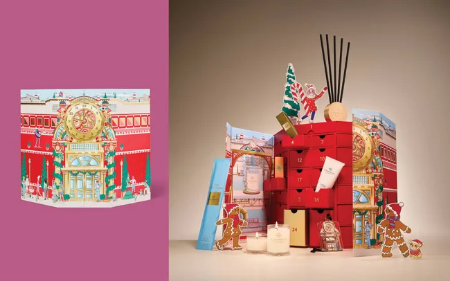 Colourful advent calendar featuring a whimsical holiday scene with multiple small drawers. Includes festive items like candles and reed diffusers, evoking a warm, celebratory mood.