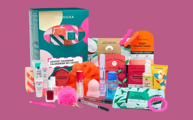 Sephora advent calendar with various beauty products: lipsticks, masks, skincare items, and accessories. Colourful packaging on a pink background.